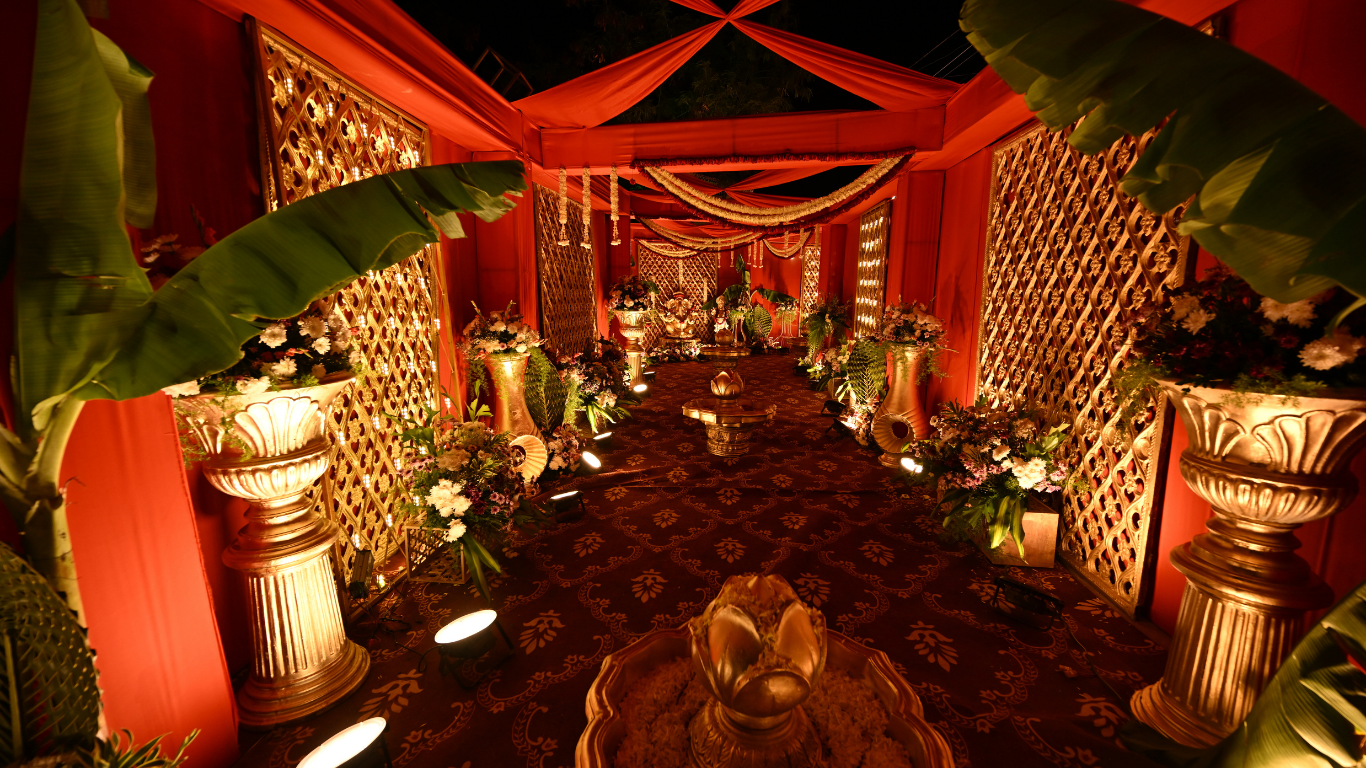Red-draped wedding pathway with golden pillars and floral arrangements